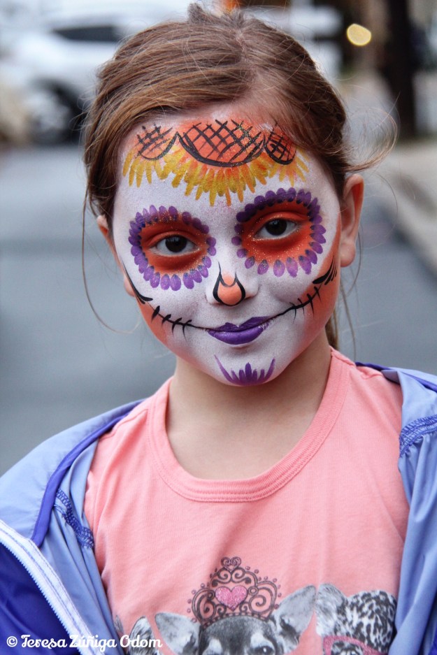 A young girl has her face painted as sugar skull at the festival.  This is one of the most popular things to do at Dia de los Muertos.